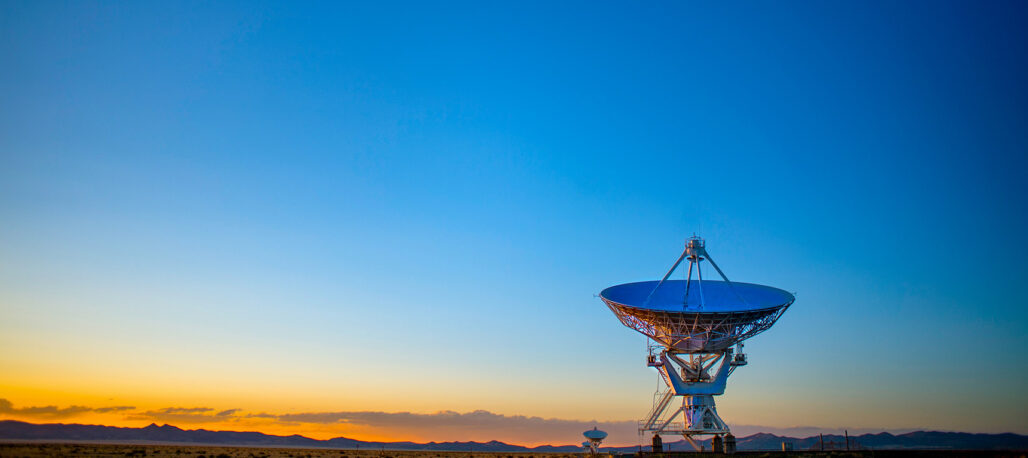 A satellite dish in a desert landscape at sunrise